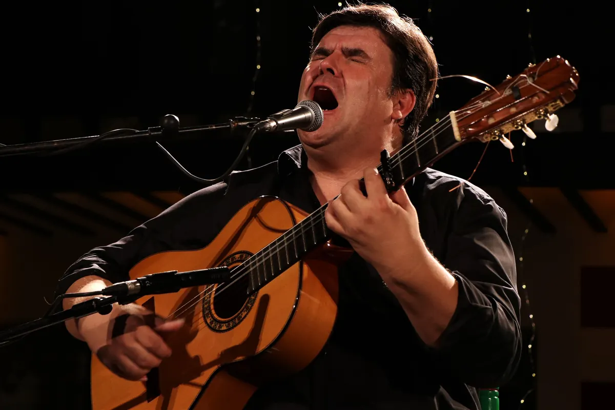 A flamenco singer with a guitar at a microphone, head tilted back as he sings